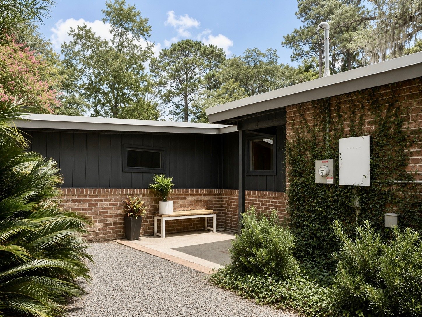 Courtyard entry with black board-and-batten siding over brick, jasmine climbing the wall beside the Tesla Powerwall